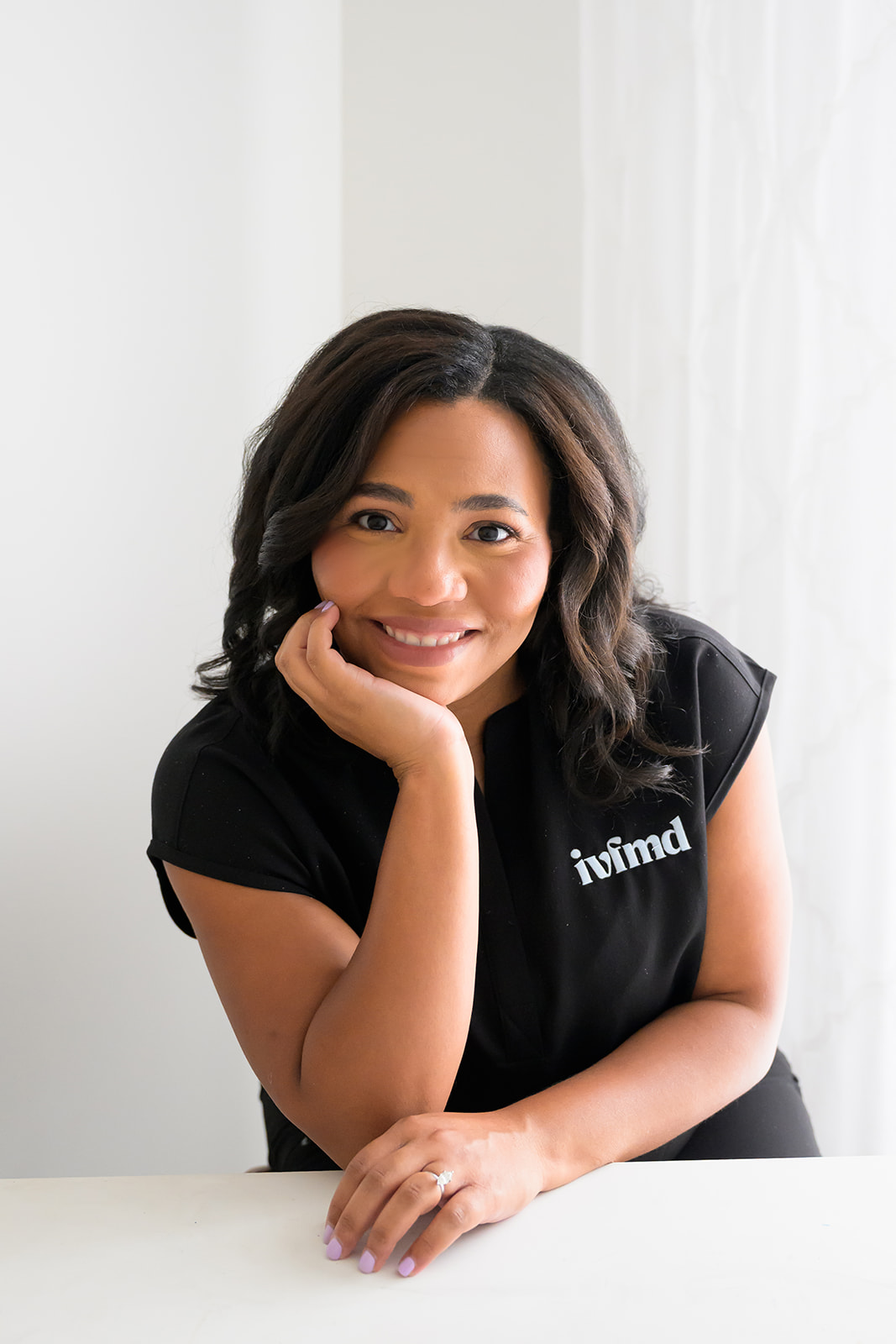 Woman in black scrubs leans on a table with her chin cupped in her hand during a business photoshoot in Houston TX