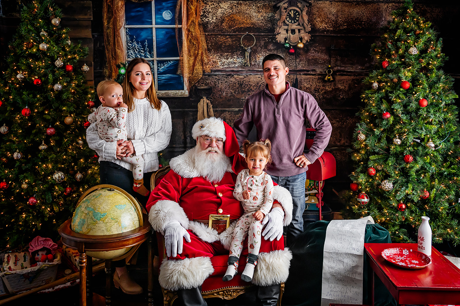 Santa seated with little girl on his knee while her parents and baby brother gather around them