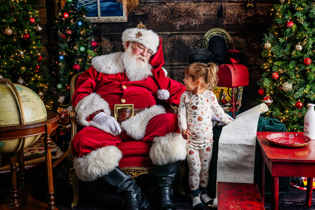 Little girl looking up at Santa while she points to her name on the Nice List