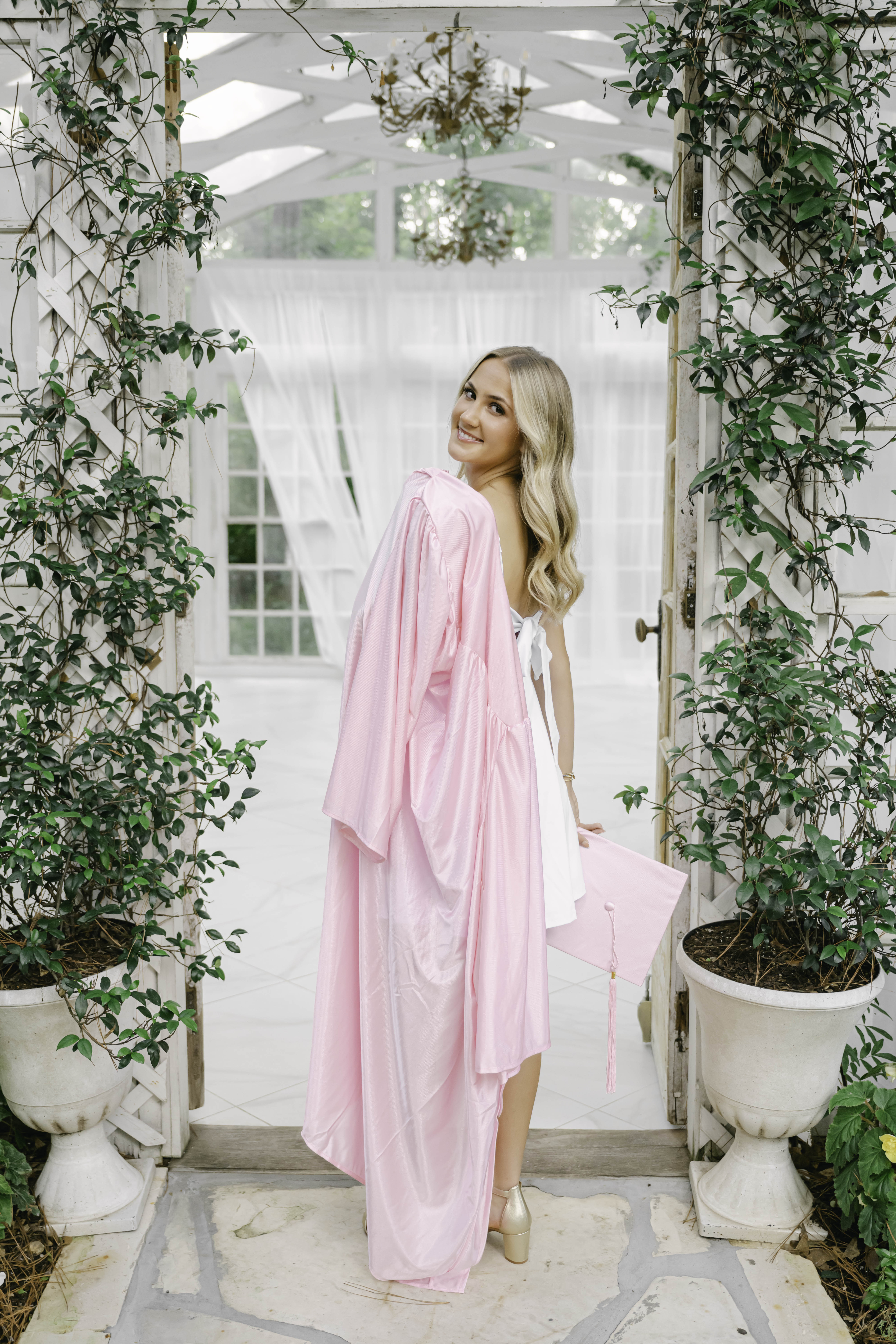 Class of 2027 senior wearing a pink cap and gown during a Houston senior portrait session